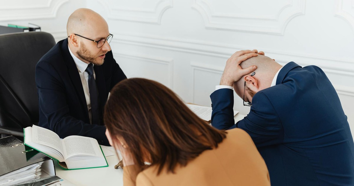 Legal professionals engaged in a tense meeting at a law office with open documents on the desk.