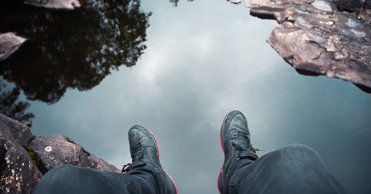 High angle view of a person sitting by water, wearing sneakers, embracing nature's tranquility.