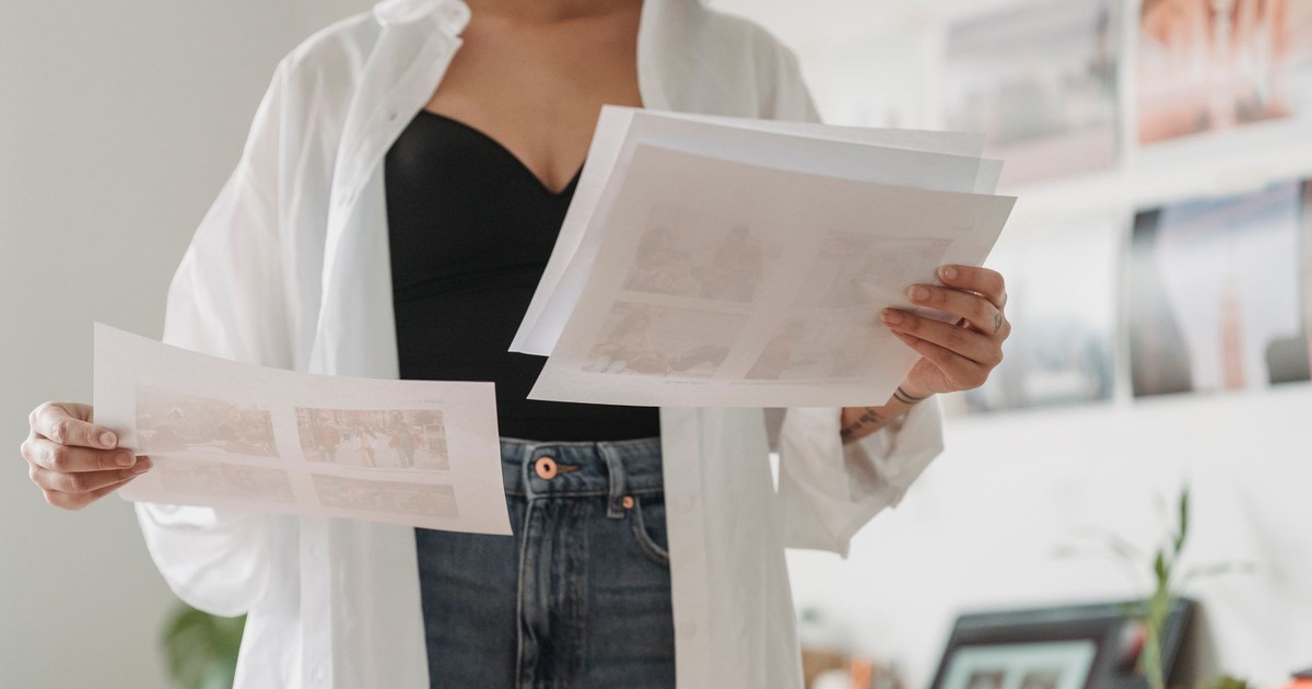 Crop anonymous female employee comparing photos on paper sheets while working on project in light house