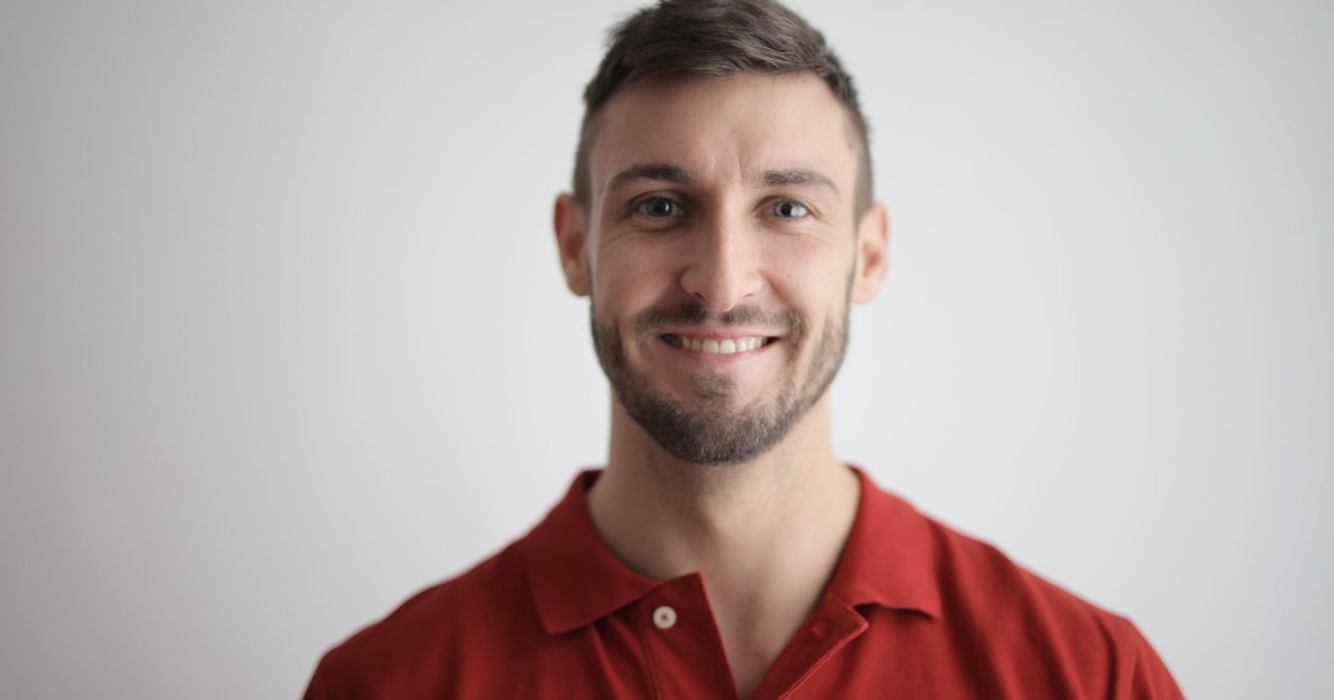 Headshot of a happy man with a beard wearing a red polo shirt against a white background.