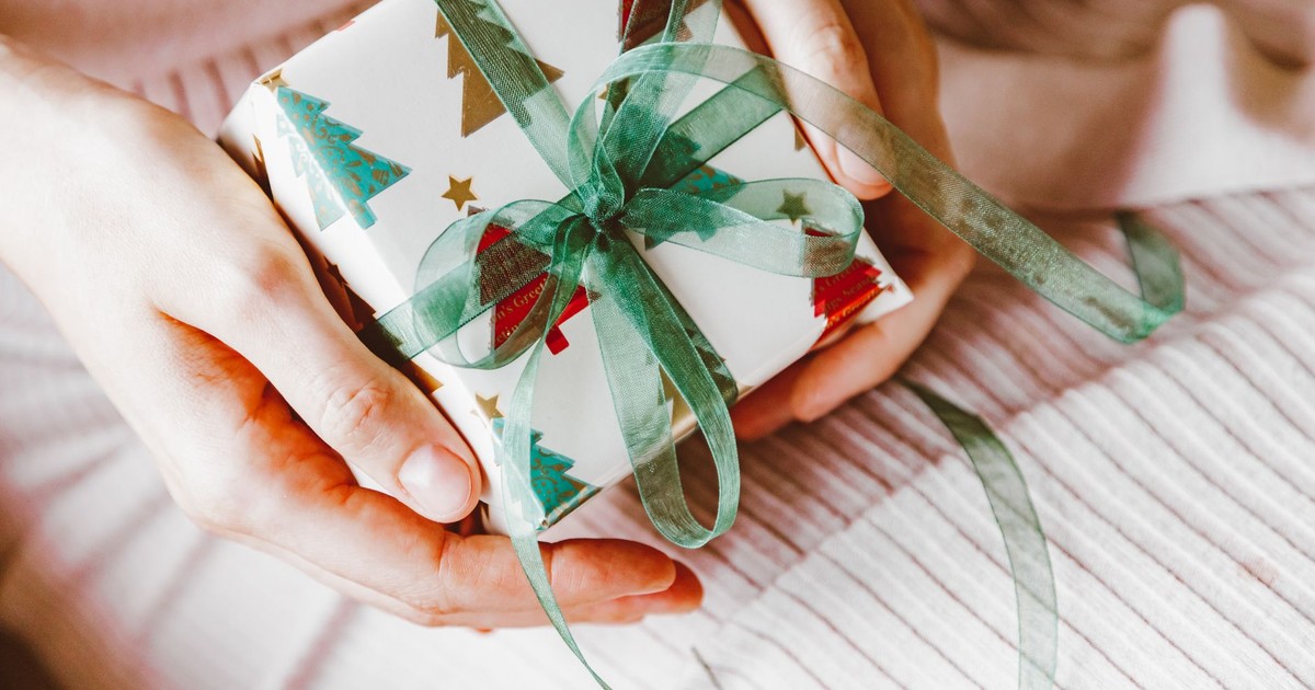 Symbolic Christmas gift wrapped in holiday-themed paper with green ribbon, held in hands.