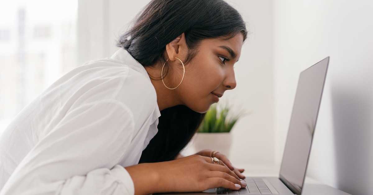 Young woman using laptop for studying, displaying focused expression and engaged posture.