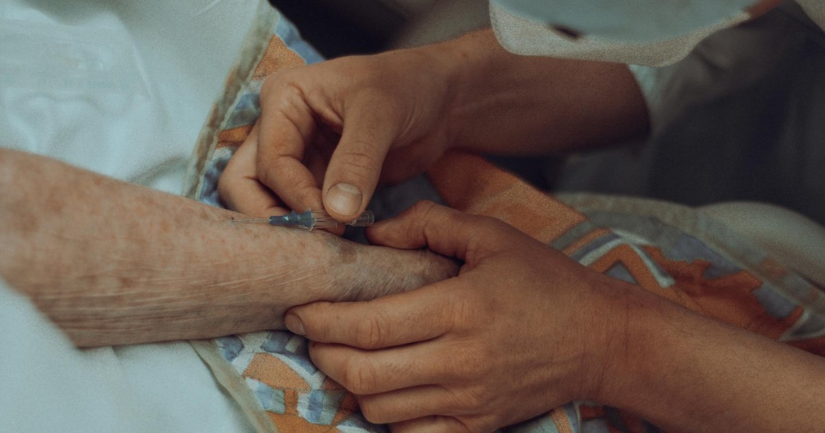 A healthcare professional administers an injection to an elderly patient in a hospital setting.