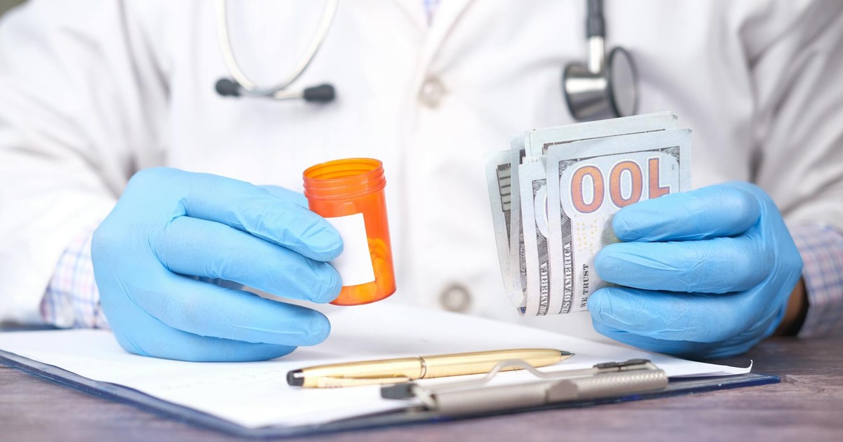 Doctor in gloves holding pill bottle and cash, highlighting medical expenses.