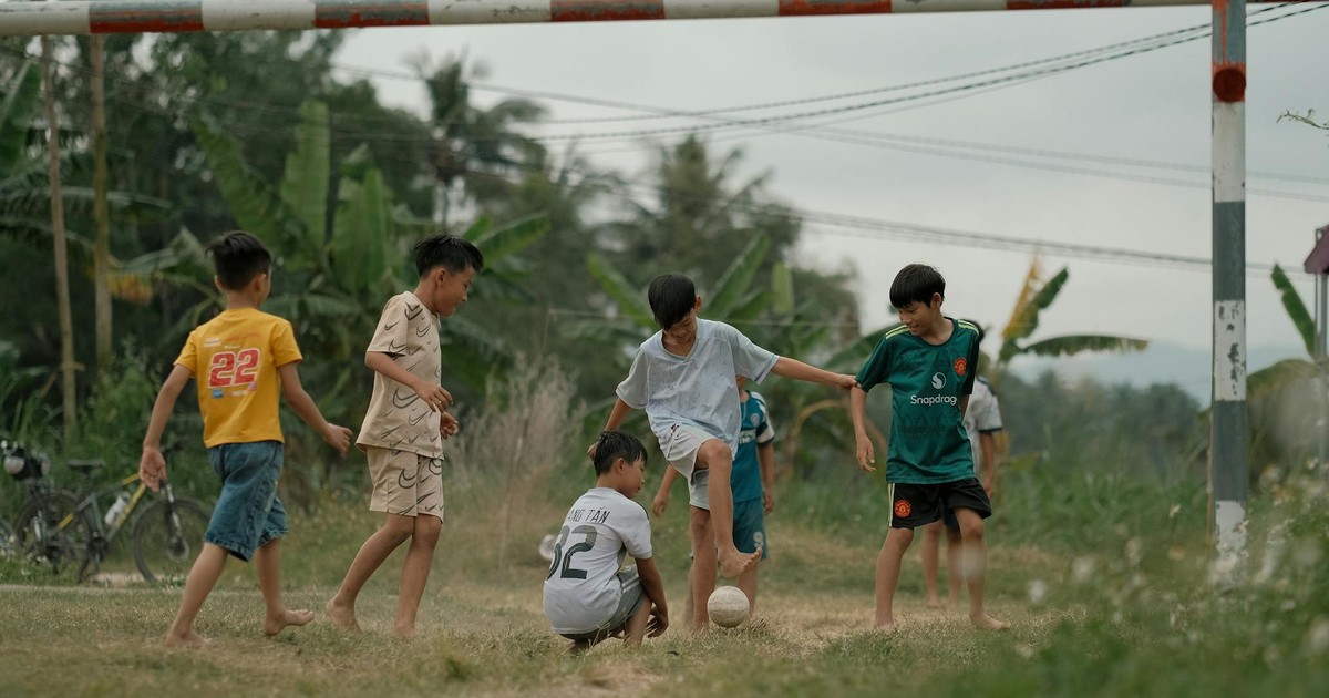 Group of boys playing soccer in a lush green field on a cloudy day.