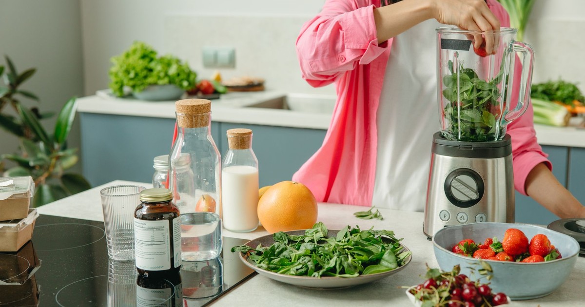 Woman in pink sleeve blending fresh fruits and veggies for a healthy smoothie.