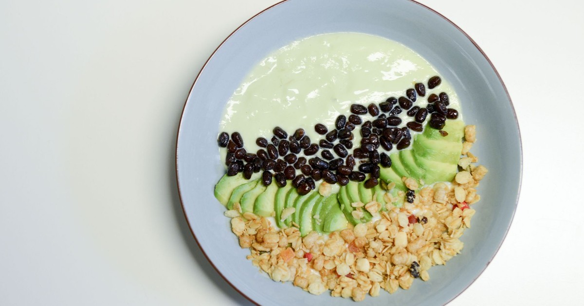 A healthy smoothie bowl featuring avocado, black beans, and granola served in a ceramic bowl.