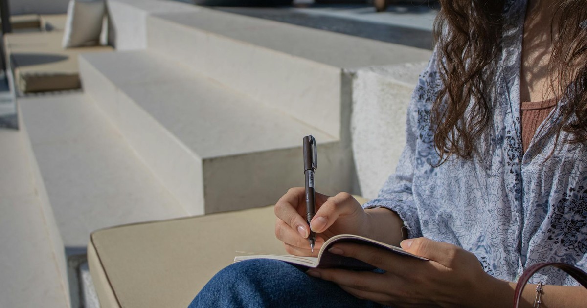 A woman sitting outdoors in daylight, writing in a notebook in İstanbul, Türkiye.