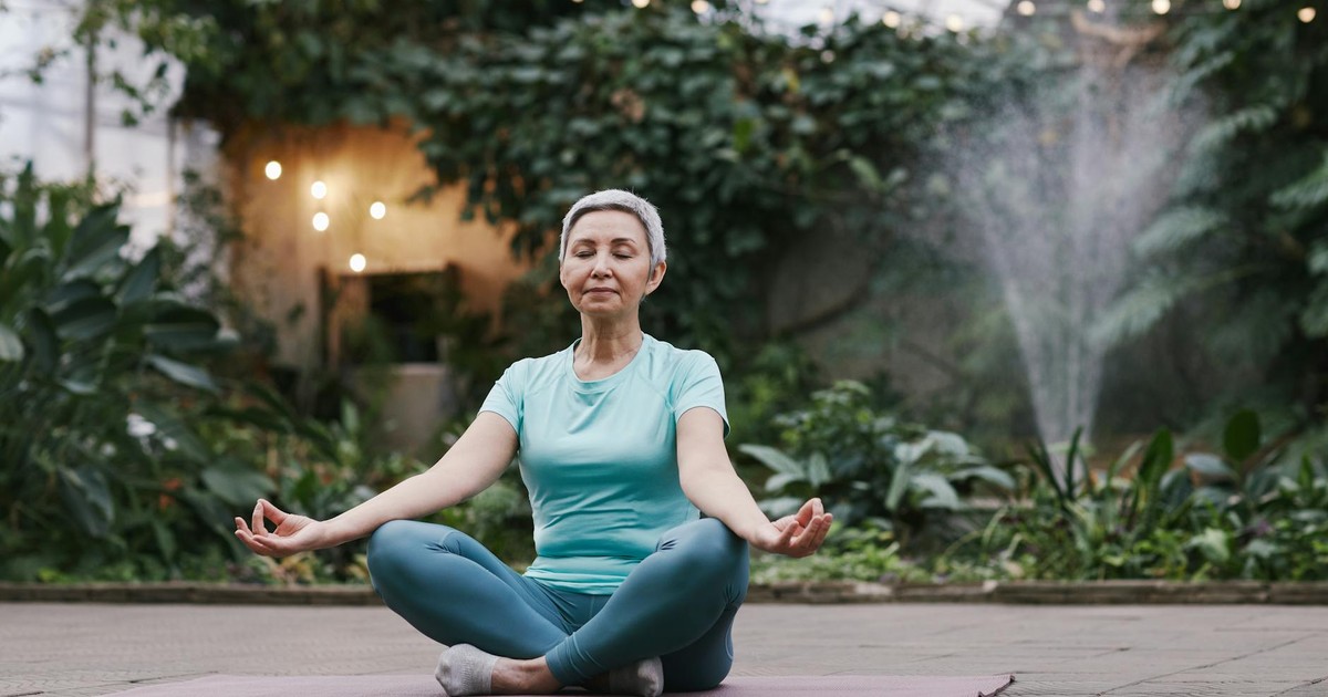Elderly woman meditating in serene botanical garden setting, focused on wellness and mindfulness.