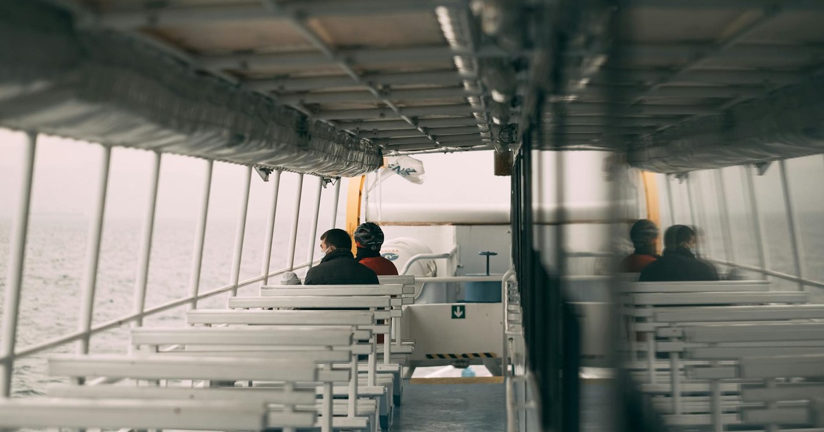 Two people enjoy a quiet ride on an empty ferry with a view of the sea.
