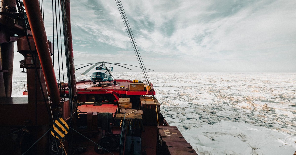 A helicopter on the deck of an icebreaker ship navigating through icy Arctic waters.