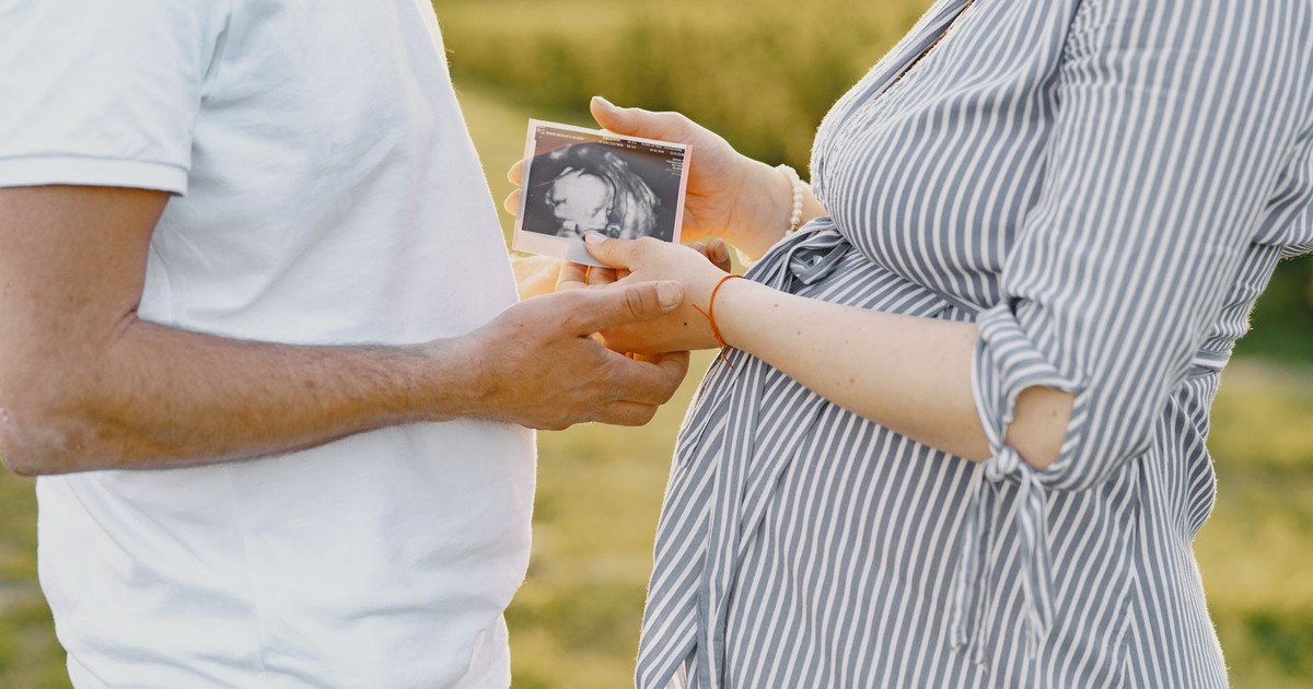 A couple holds an ultrasound image, representing pregnancy and family love, in an outdoor setting.