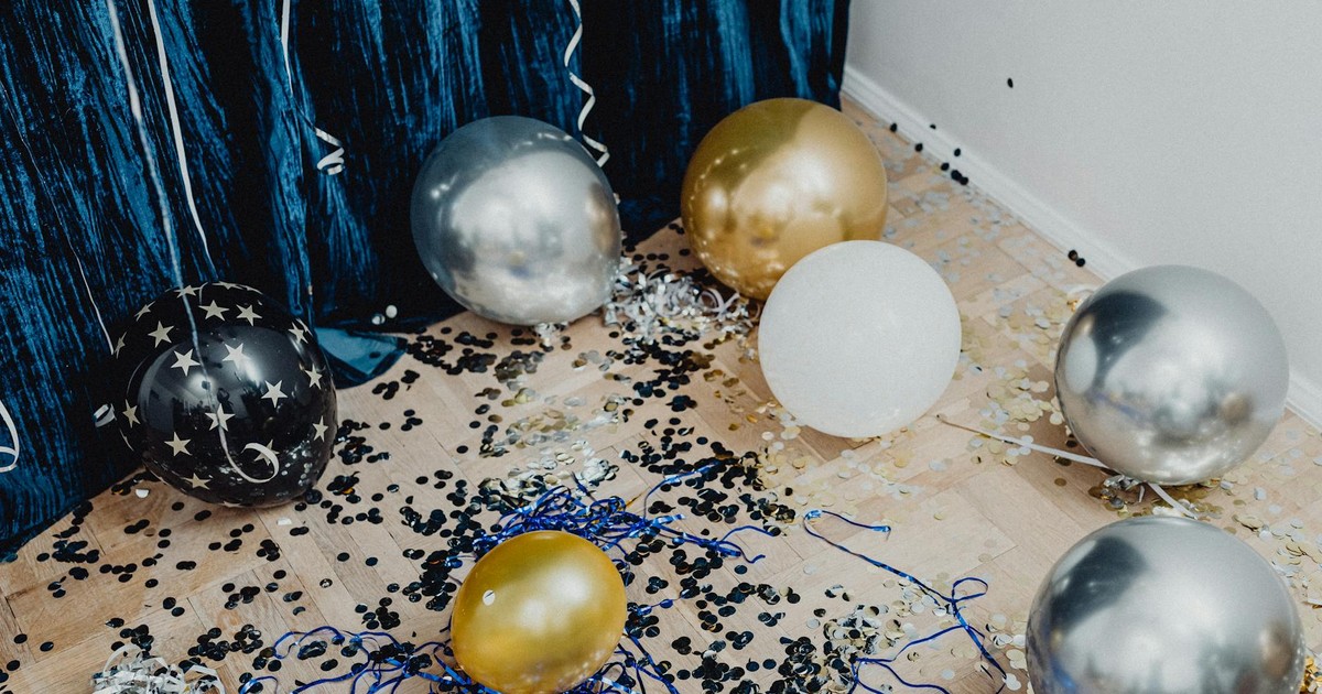 Festive arrangement with gold, silver balloons and confetti on wooden flooring.