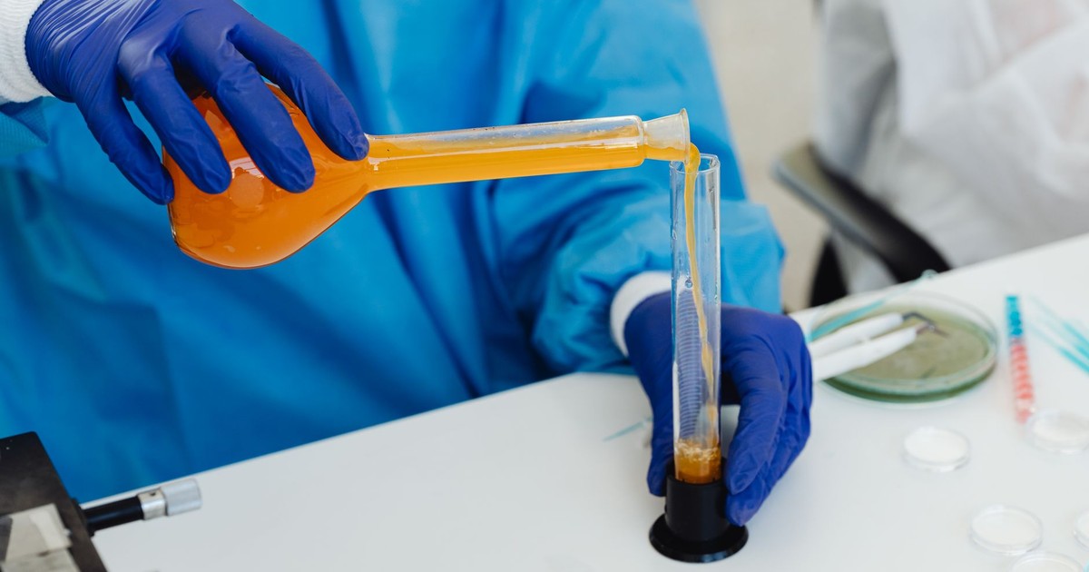 Close-up of a scientist pouring orange liquid into a vial in a laboratory setting.