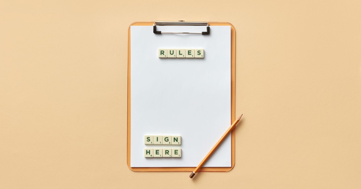 Flat lay of clipboard with letter tiles spelling 'rules' and 'sign here', accompanied by pencil on beige background.