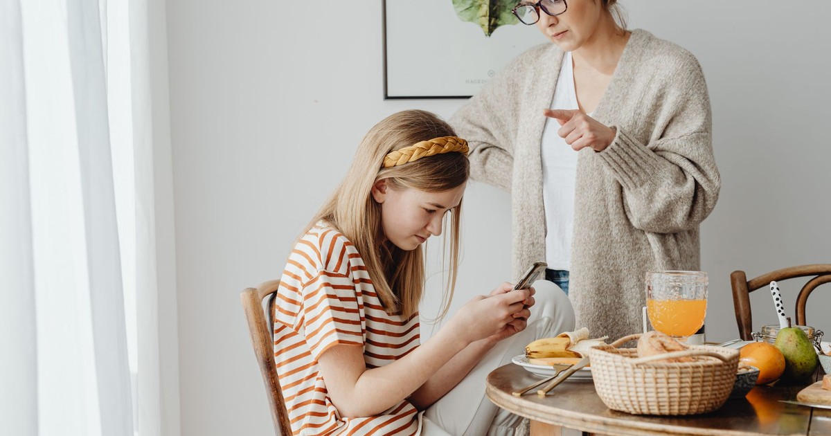 A mother scolds her teenage daughter for using a cellphone during breakfast at the dining table.