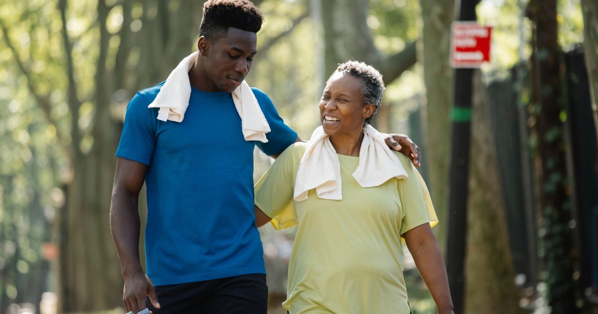 An elderly woman and young man walk arm in arm, smiling in a park. Active lifestyle.