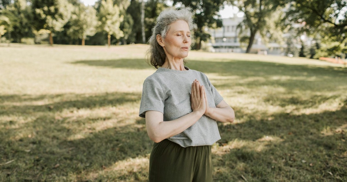 Elderly woman meditating and practicing yoga in a sunny park, embracing wellness and mindfulness.