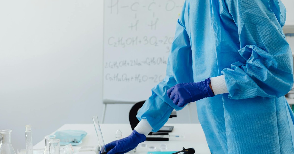Scientist in protective clothing working in lab with chemical formulas on whiteboard.