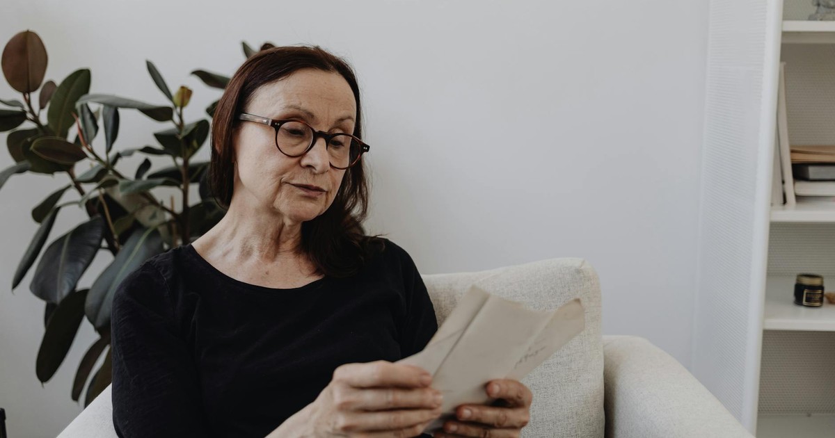 Senior woman sitting in an armchair indoors, reading letters, reflecting on memories and emotions.