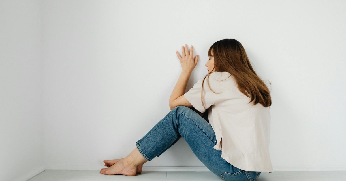 A contemplative woman sitting barefoot against a white wall, conveying solitude.