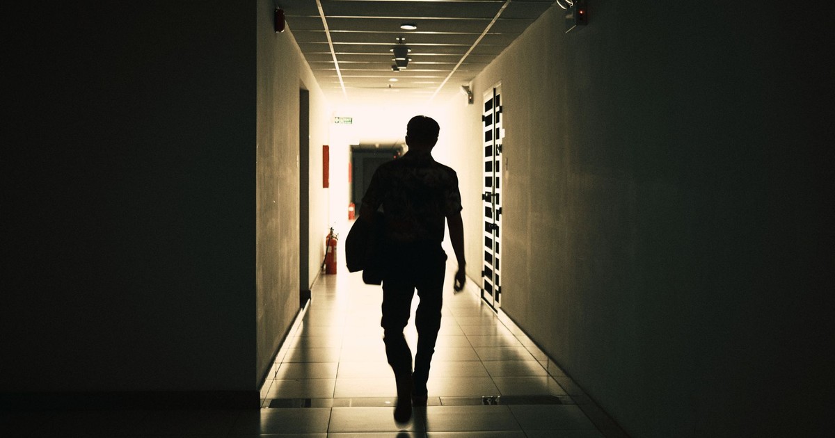 Back view silhouette of unrecognizable male walking on narrow empty hall of modern building