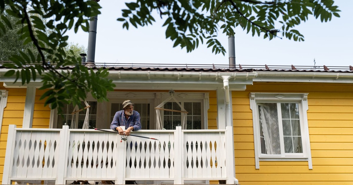 A senior man enjoys a quiet moment on a yellow country house balcony with a fishing rod.