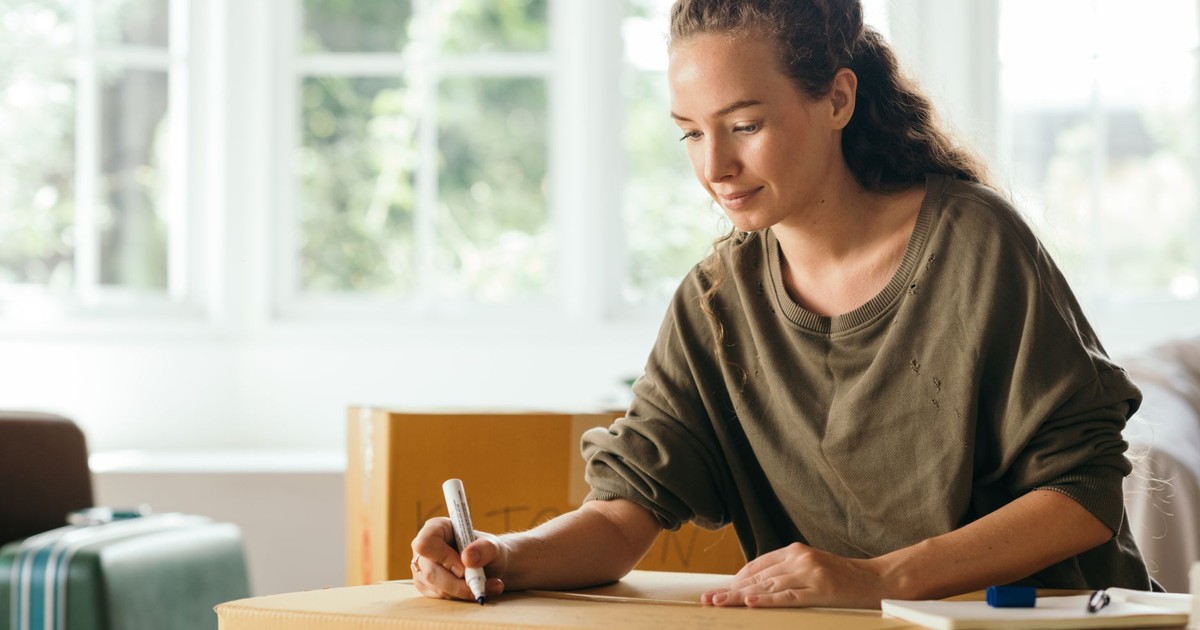 Calm lady sitting on sofa and signing box with belongings in cozy house in sunny day while moving out