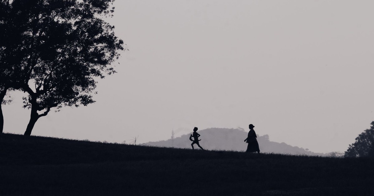 A child runs playfully with an adult in a scenic silhouette against a hilly backdrop. Captured in natural setting.