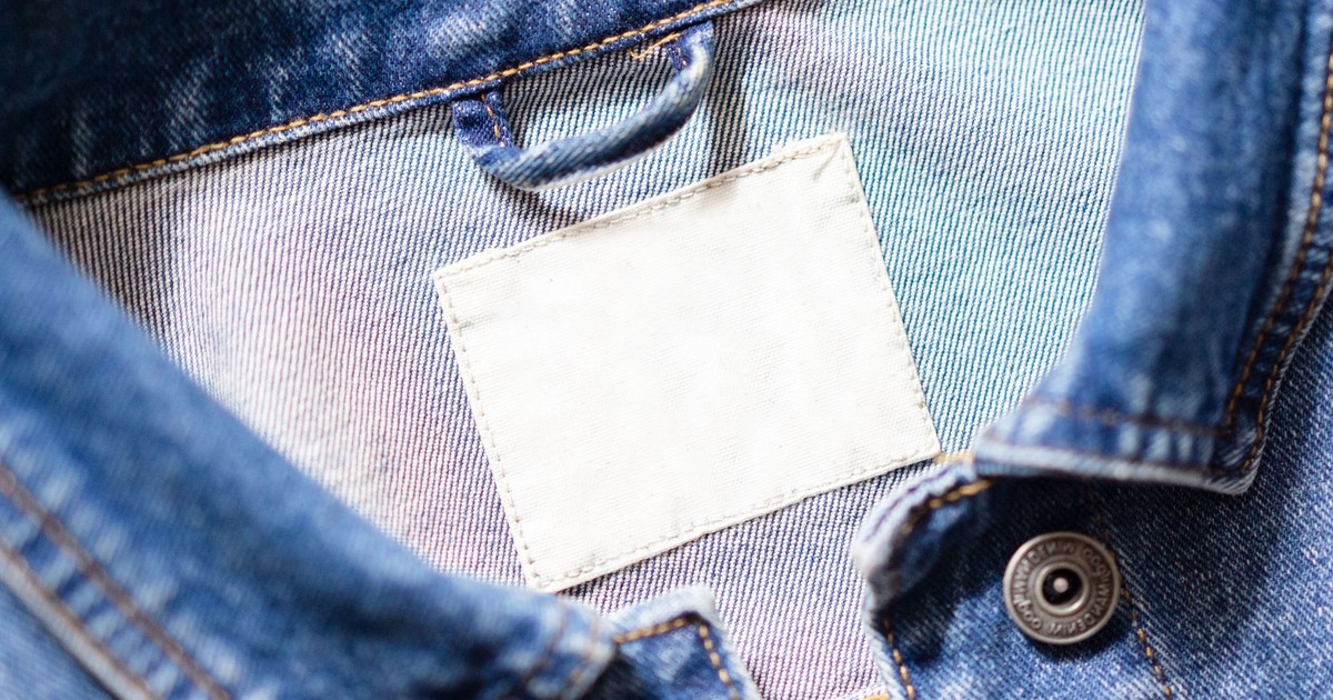 Close-up shot of a denim jacket's collar featuring a blank white tag and detailed stitching.