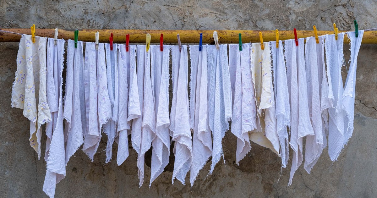Neatly arranged white fabrics drying under the sun, held by colorful clothespins against a rustic wall.