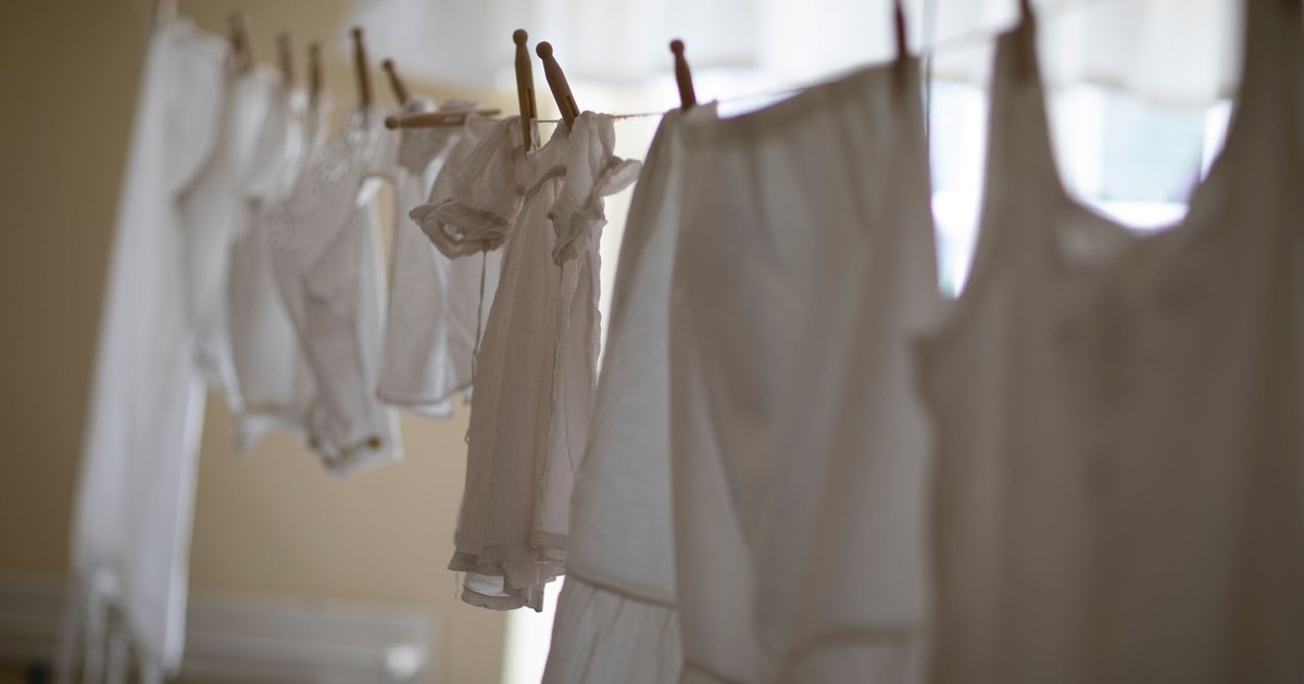 A row of white clothing hangs on a clothesline indoors, softly lit.
