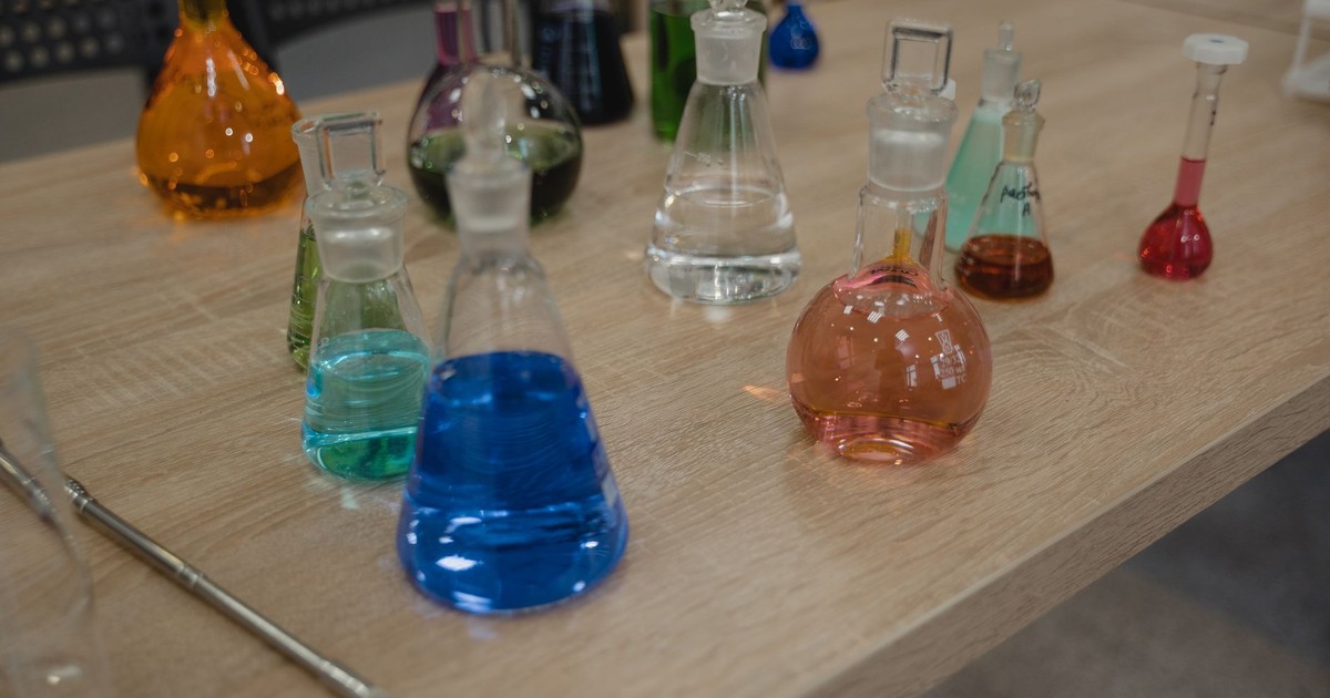 Colorful laboratory flasks with various liquids on a wooden desk for science experiments.