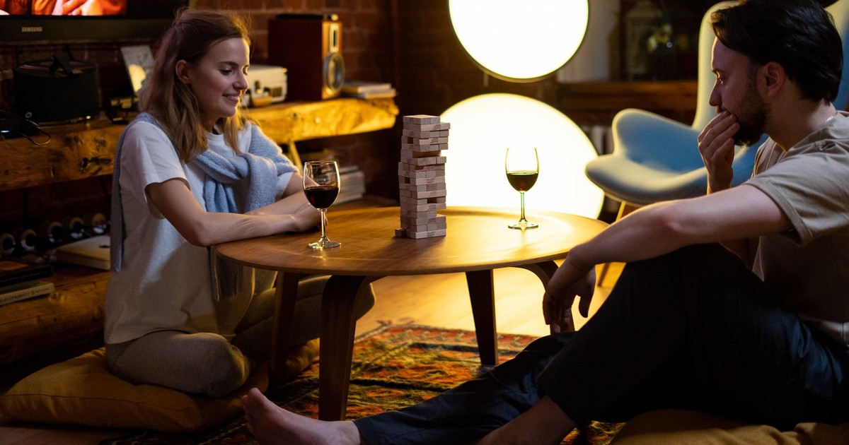 Couple playing Jenga with glasses of wine in a cozy home setting during the evening.
