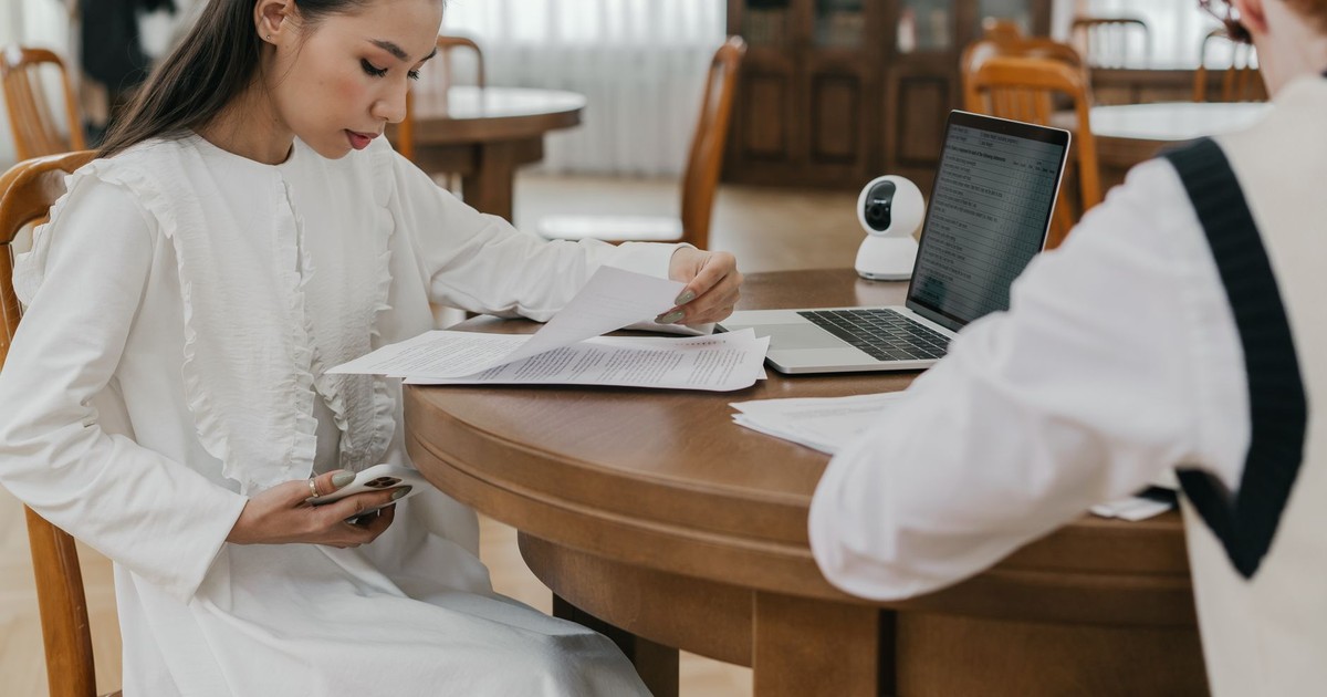 Two students focusing on their studies at a communal table, using laptops and documents.