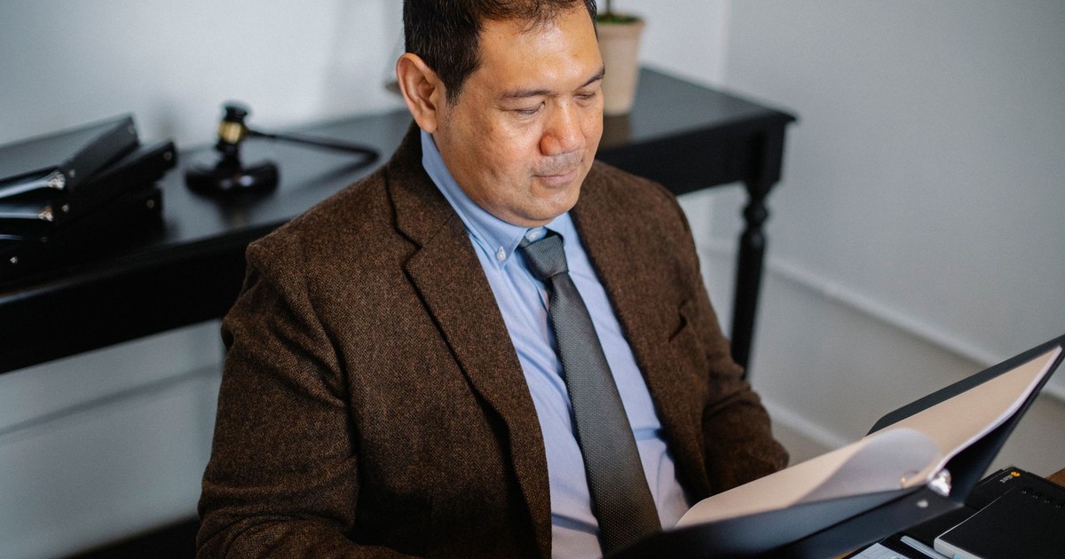 From above of serious ethnic lawyer in elegant suit checking report in folder on blurred background of office