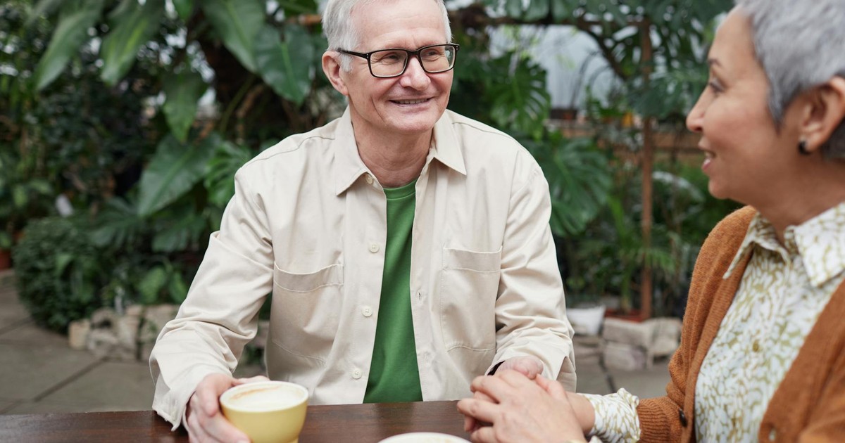 Happy senior couple sharing coffee and conversation in a lush garden setting.