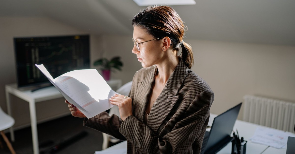 Professional woman in glasses reviewing financial documents at her office desk.