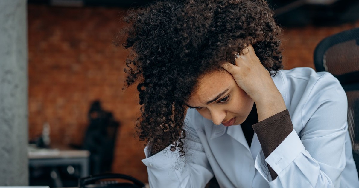 A woman in an office appears stressed while reviewing documents at her desk.