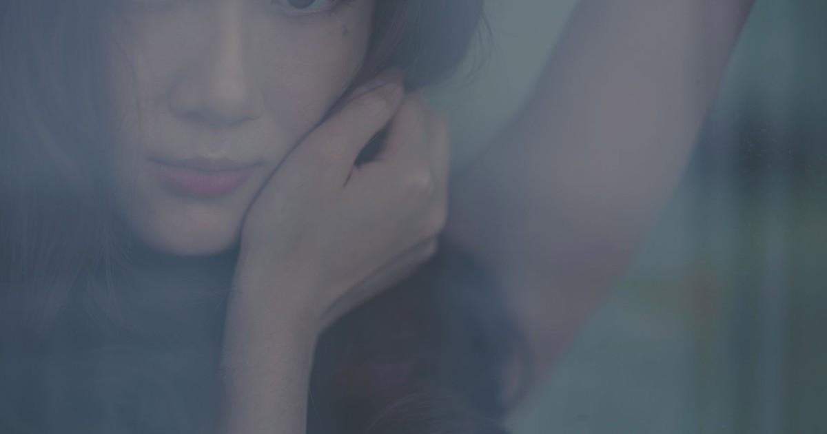Artistic portrait of a young woman gazing through a window with a thoughtful expression.
