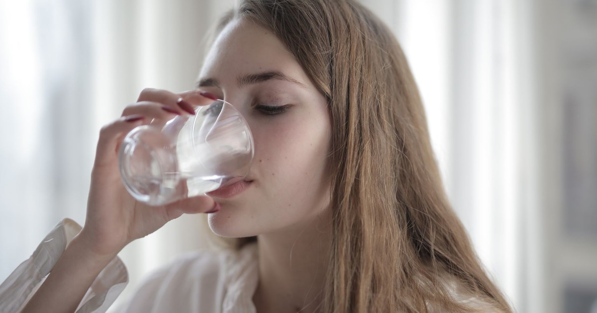 A woman enjoying a refreshing glass of water indoors during the day.