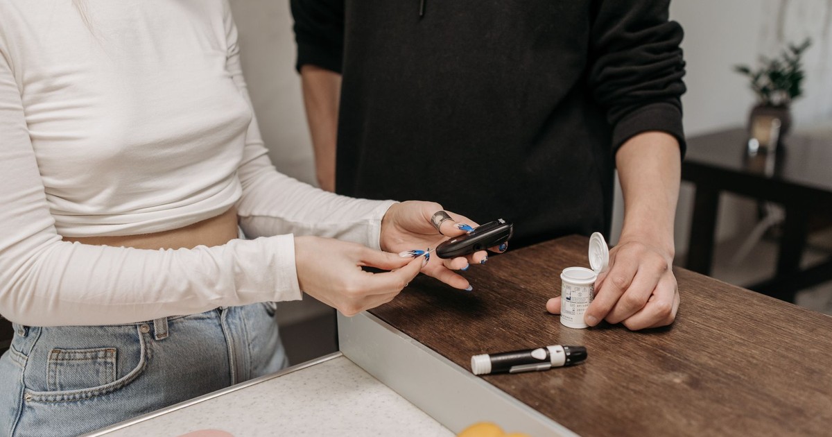 Two adults checking blood sugar with a glucometer and insulin pen on a wooden table.