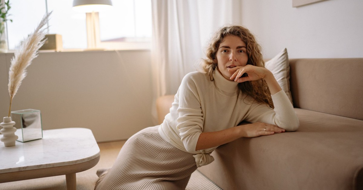 A woman leans on a sofa in a chic, cozy minimalist interior space.
