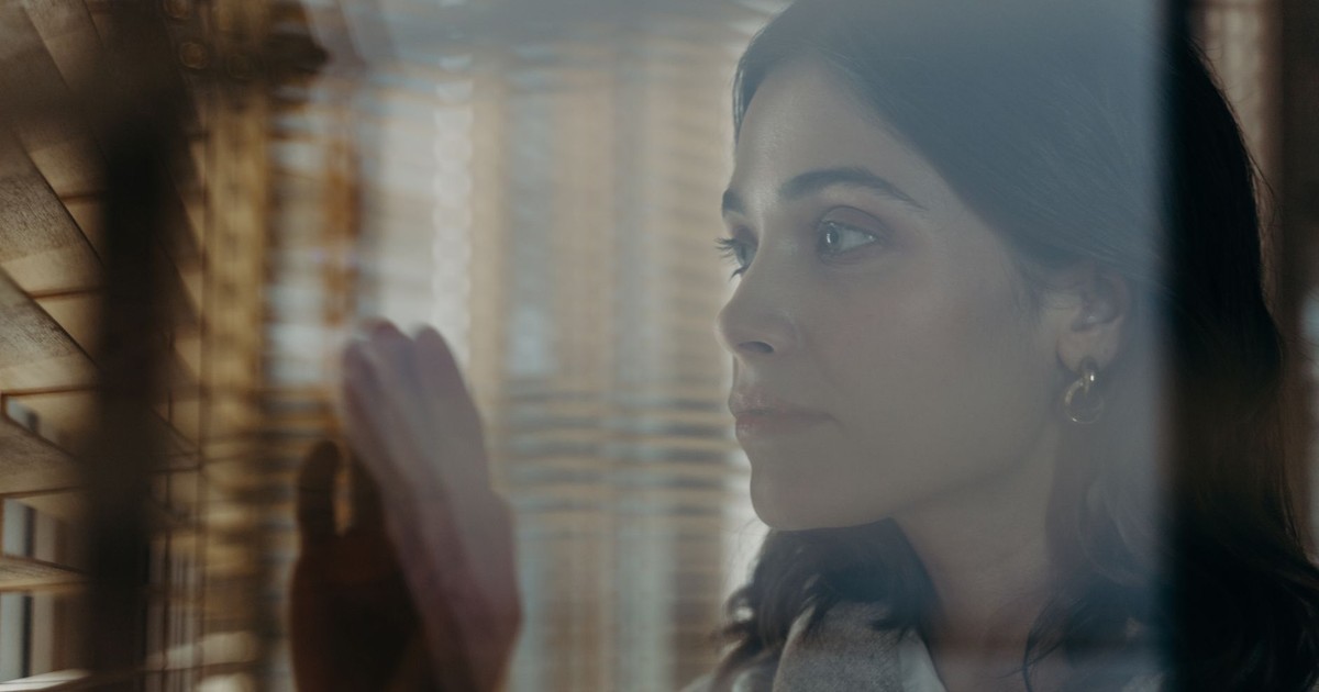 A thoughtful woman peeks through window blinds, creating a contemplative mood.
