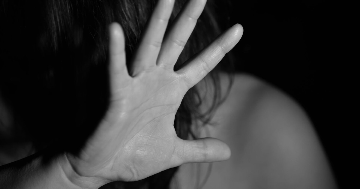 A black and white photo of a woman raising her hand, obscuring her face, suggesting a stop gesture.