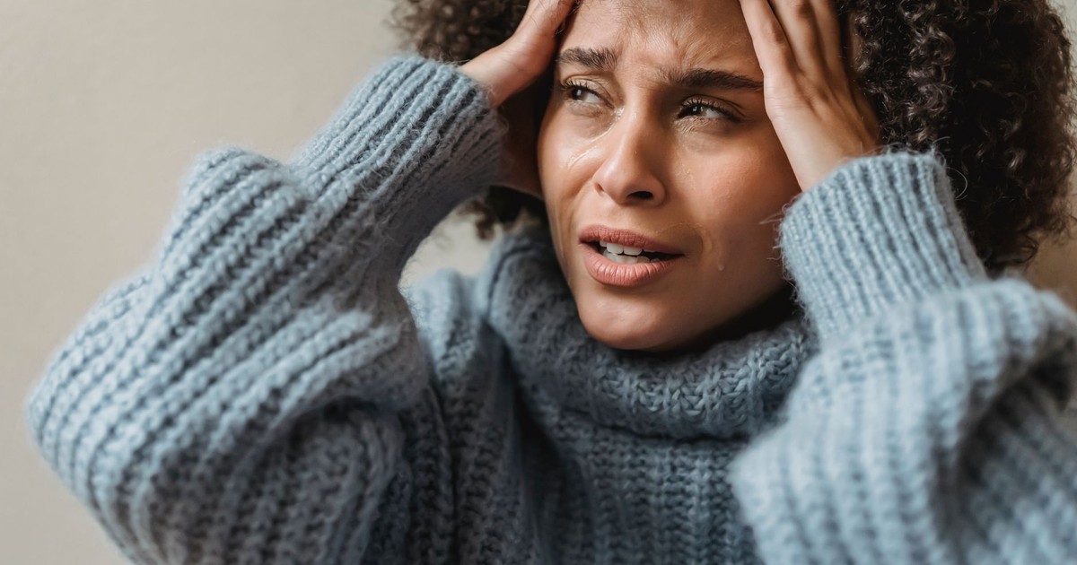 Worried African American female with brown curly hair crying and touching head against light wall