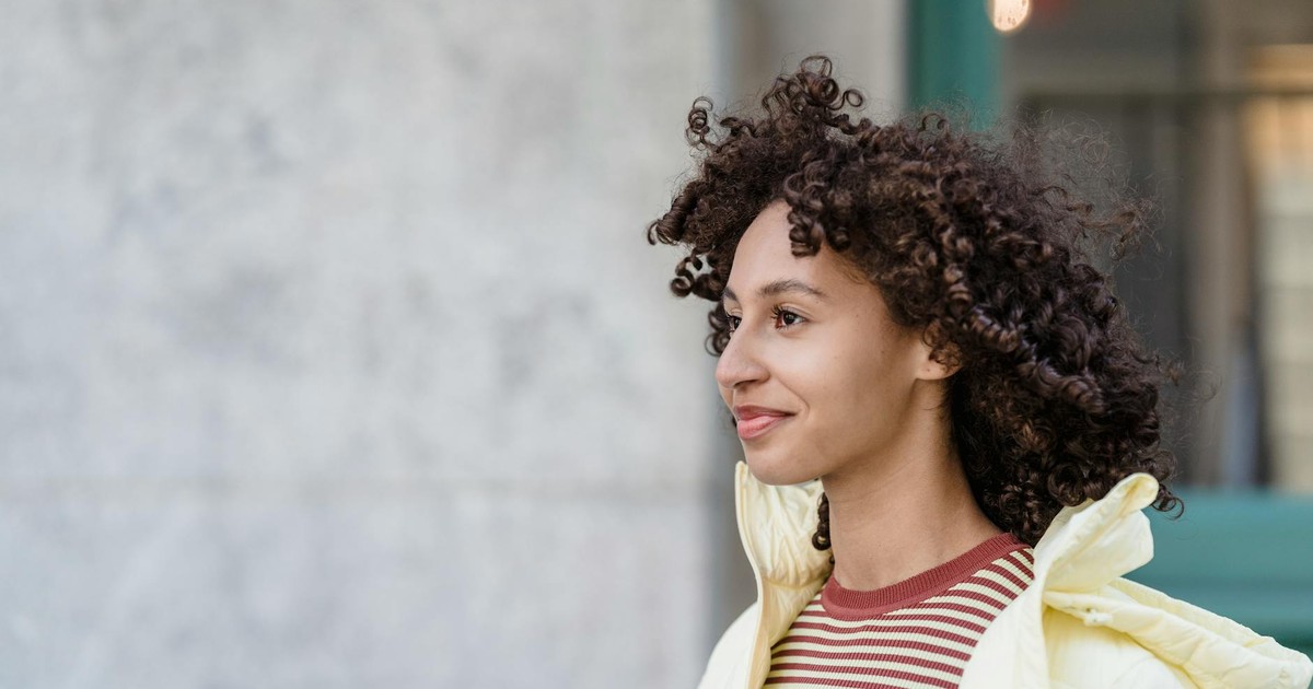 Satisfied young ethnic female in striped wear and jacket looking forward on city street in daytime