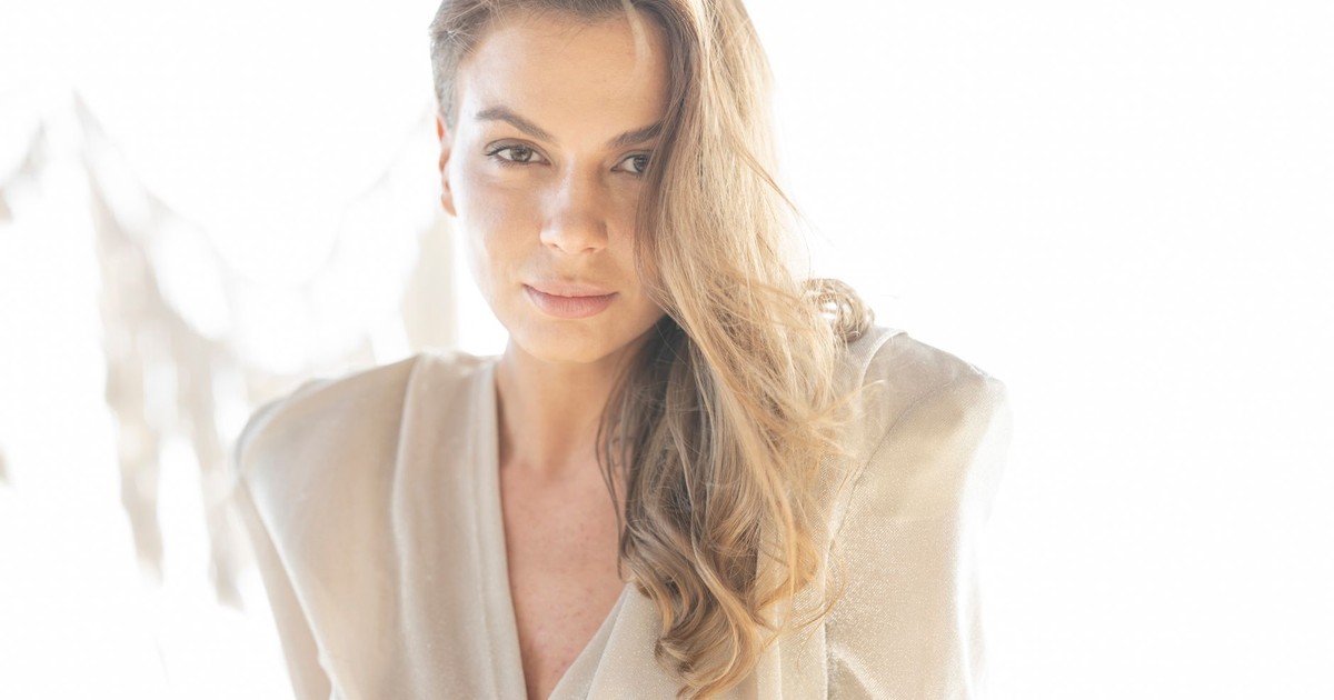 Close-up portrait of a woman with long hair and stylish outfit in soft lighting.