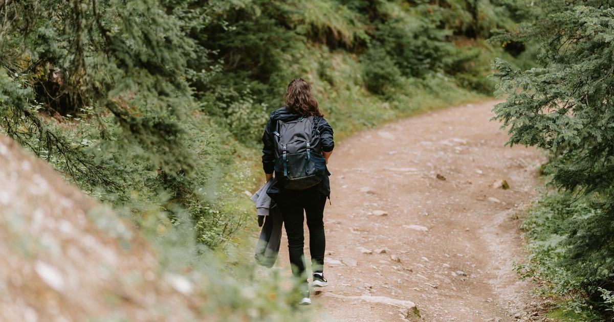 A woman hiking with a backpack on a scenic dirt road in Banff, surrounded by lush trees.