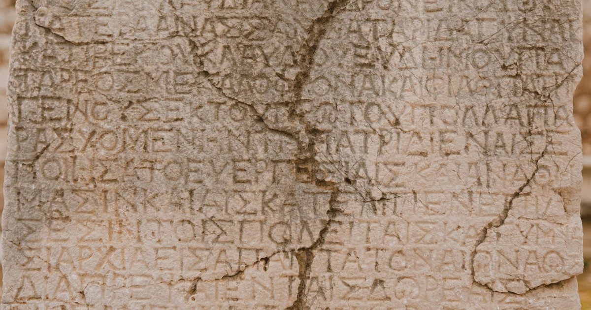 Close-up of a weathered stone with ancient Greek letters inscribed, showcasing historical text.
